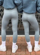 Two people wearing gray leggings and white sneakers on a brick pavement.