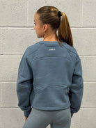 Person wearing a blue sweatshirt with 'Darcy' branding against a gray brick wall.
